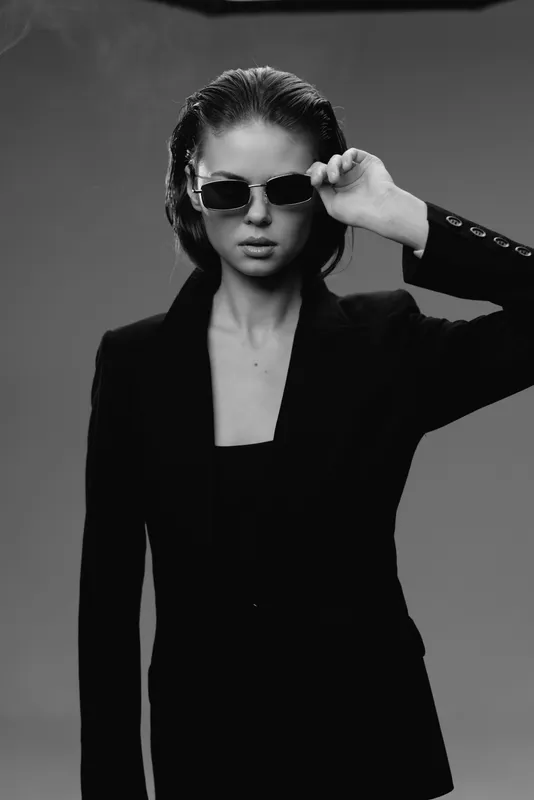 Black and white portrait of stylish woman in sunglasses wearing black jacket with serious expression