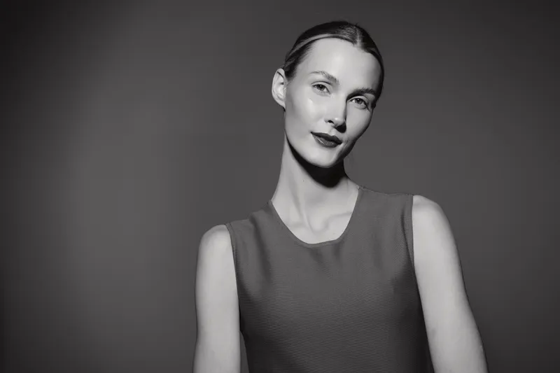 Portrait of a young white woman with light skin and slicked back hair wearing a sleeveless top. Studio shot with soft lighting on a dark grey background. Concept of elegance and confidence.