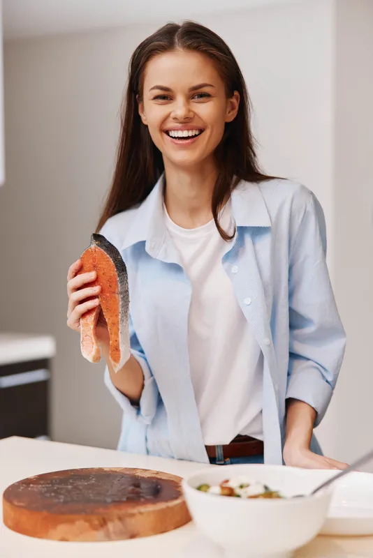 Счастливая женщина готовит свежее филе лосося на кухне для вкусного обеда