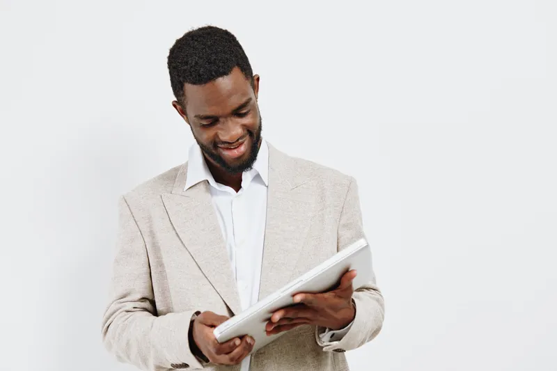 Smiling man holding tablet device in casual beige cardigan and white shirt, reading or browsing, positive mood, indoor studio shot, natural lighting, everyday lifestyle concept