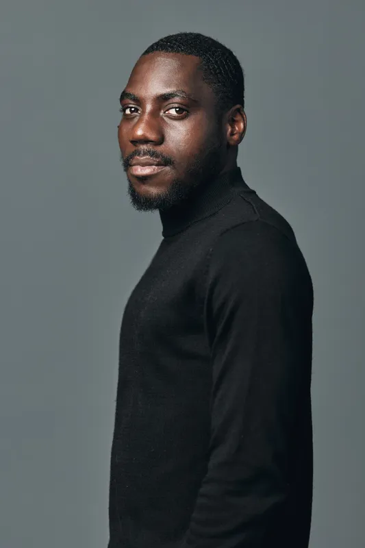 Portrait of African American man with dark skin wearing black turtleneck sweater looking at camera with confident expression in creative visual designer style on gray background.