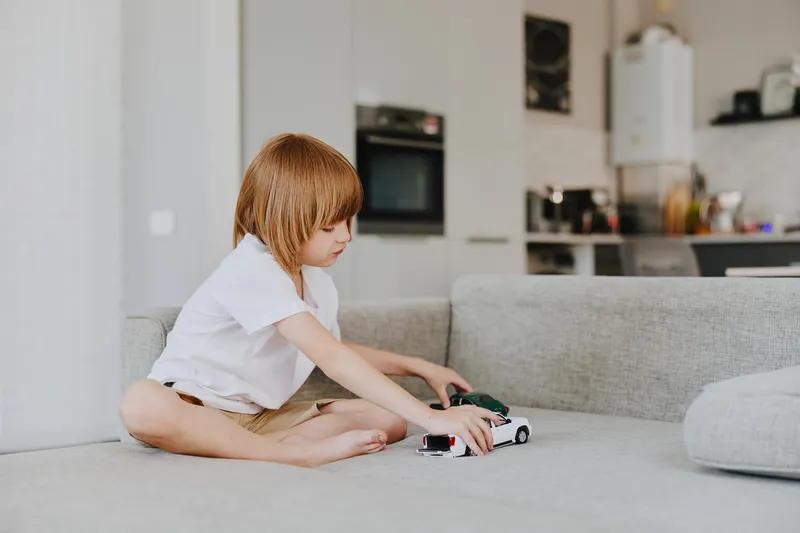 Young boy playing with toy cars, focused on creativity and fun, exploring his imagination with colorful miniature vehicles in a cozy living room.