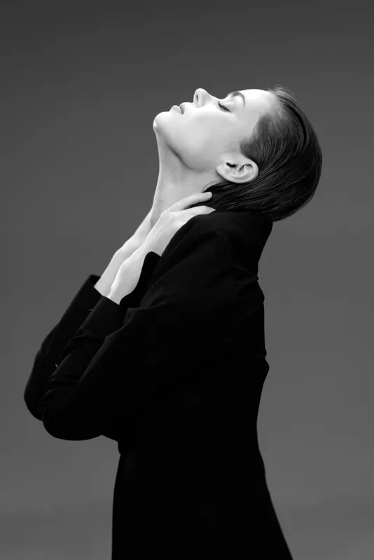 Black and white portrait of a thoughtful woman in a black outfit with closed eyes and elegant pose.