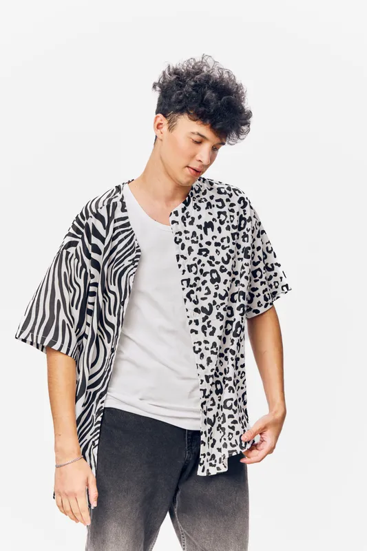 young man wearing a stylish black and white animal print shirt, standing against a bright white background with a thoughtful expression and casual outfit