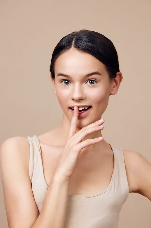 Young female model with a playful expression, wearing a nude top, with a soft background, showcasing natural beauty and confidence, ideal for lifestyle and beauty concepts