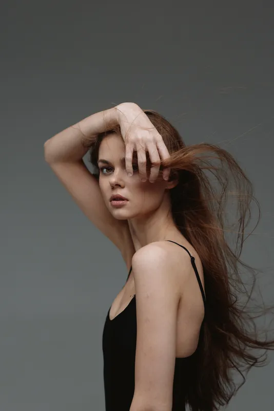 slender woman with flowing hair posing against gray background in black dress