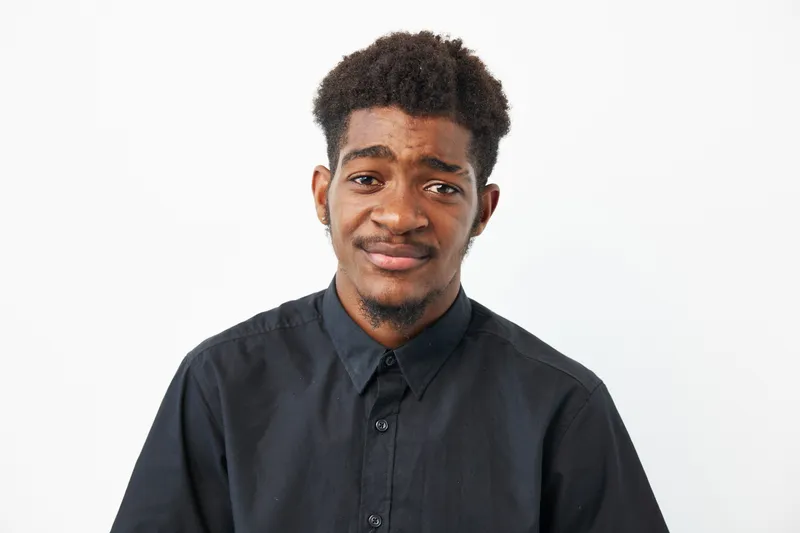 A thoughtful black man expresses genuine emotions in a minimalist studio setting. Soft lighting highlights his features, creating an intimate atmosphere.