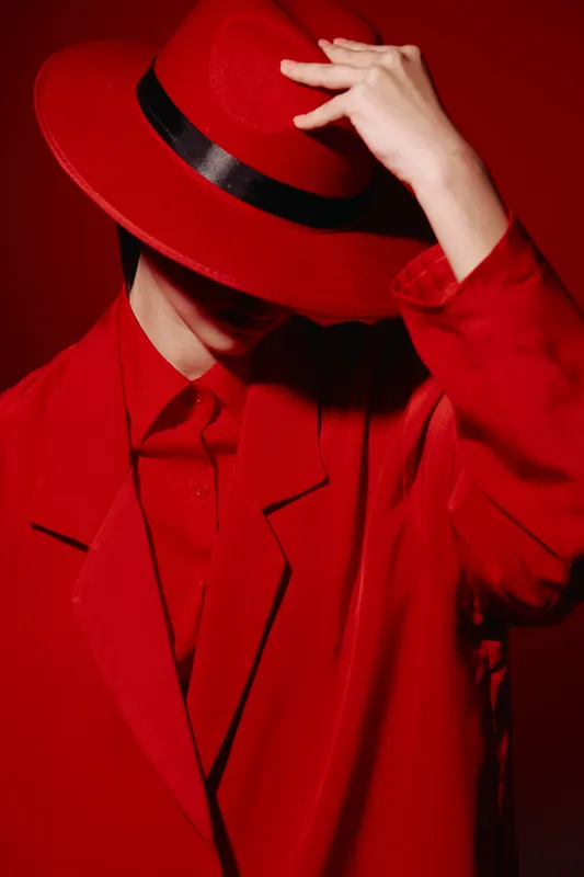 Fashionable person in vibrant red coat and matching wool hat faces down posing stylishly. The deep red tones create a bold creative beauty concept for modern fashion editorial.