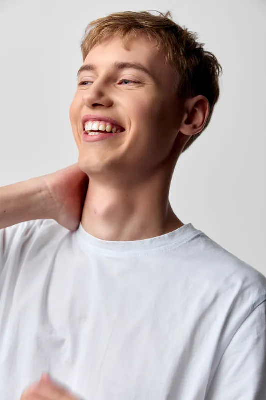 Smiling man wearing a white shirt in a candid, cheerful moment, conveying joy, confidence, and relaxed style for lifestyle and fashion visuals with bright lighting