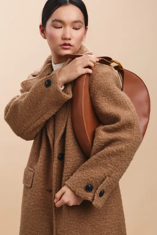 asian woman wearing a chic coat adjusts a leather backpack in a studio, projecting confident style and a modern urban fashion mood for a versatile lifestyle theme.