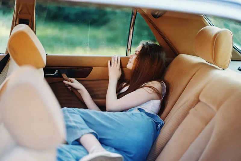 Calm young woman relaxing in a vintage car interior, enjoying a peaceful moment during a sunny day, showing comfort and nostalgia.