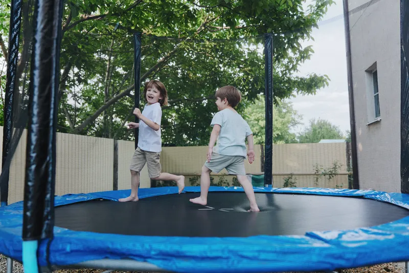 Joyful children jumping on a trampoline, enjoying outdoor fun and laughter in a sunny neighborhood setting, surrounded by greenery and happiness.