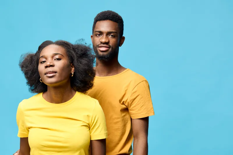 Young African couple in matching yellow T shirts, posing confidently against a bright blue background, conveying happiness and connection in a vibrant, modern style