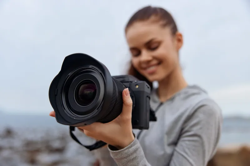 Young woman smiling while holding a camera outdoors, showcasing a passion for photography and nature, with soft natural lighting and a serene background