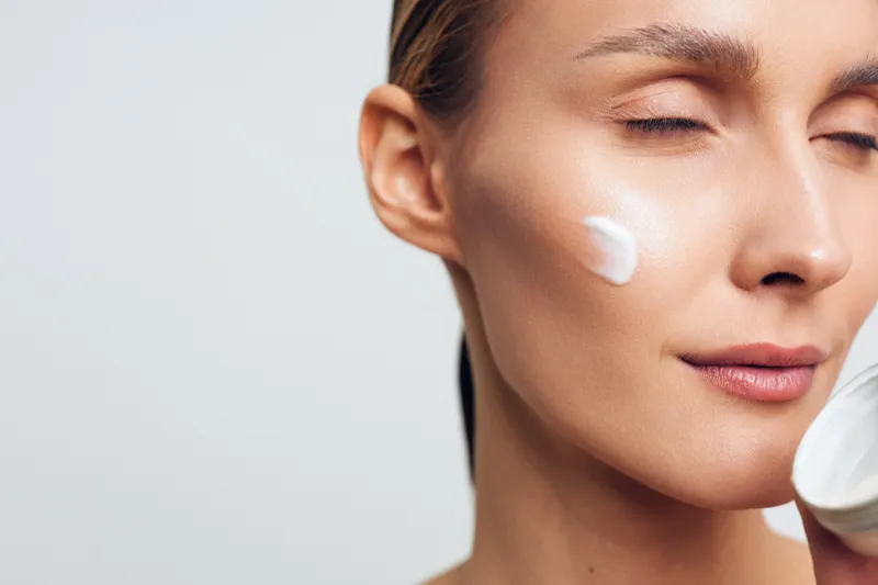 A focused woman applies cream to her cheek in a close up, calm mood as a skincare routine unfolds in a clean, minimal setting.