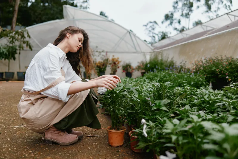 Young female gardener caring for plants in a greenhouse, dressed in casual attire, showcasing a connection with nature and sustainable living in a green environment