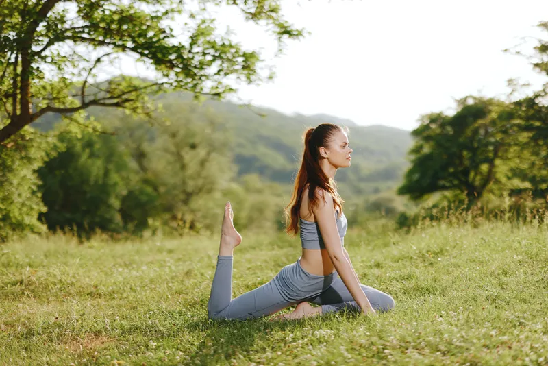 Graceful young woman practicing yoga in a serene outdoor setting, showcasing flexibility and tranquility during a sunny day in nature
