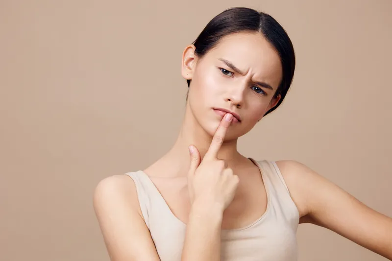 Thoughtful young woman pondering a question with a perplexed expression on a beige background, showcasing curiosity and contemplation