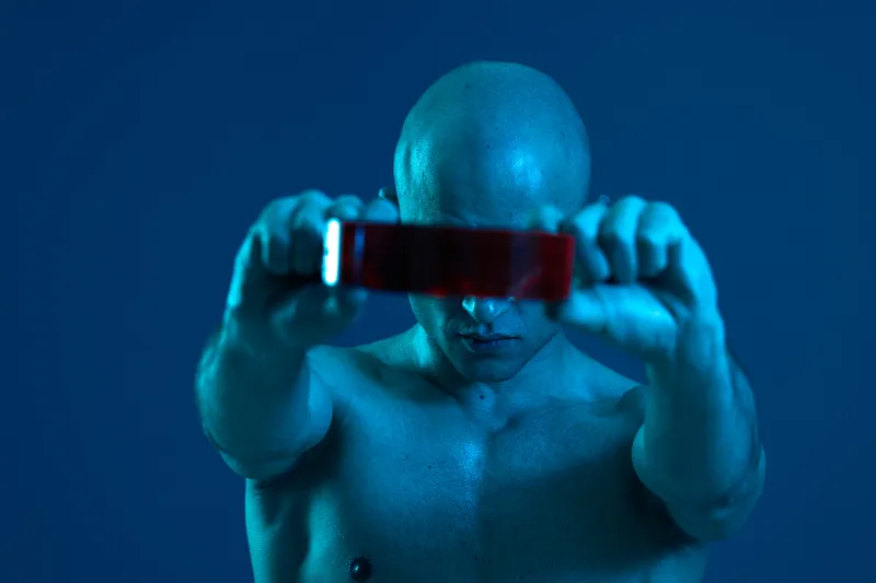 Strong man holding a red object in a dark blue atmosphere. The lighting creates an intriguing contrast, enhancing the mood of the composition while maintaining a focus on strength.