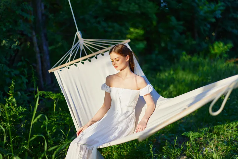 Young woman in a white dress relaxing in a hammock, surrounded by lush greenery, evoking serenity and connection with nature, perfect for wellness and relaxation themes