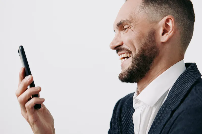 Professional man in business attire smiles while checking a mobile device on a bright isolated colorful background, conveying confident emotion and active communication.