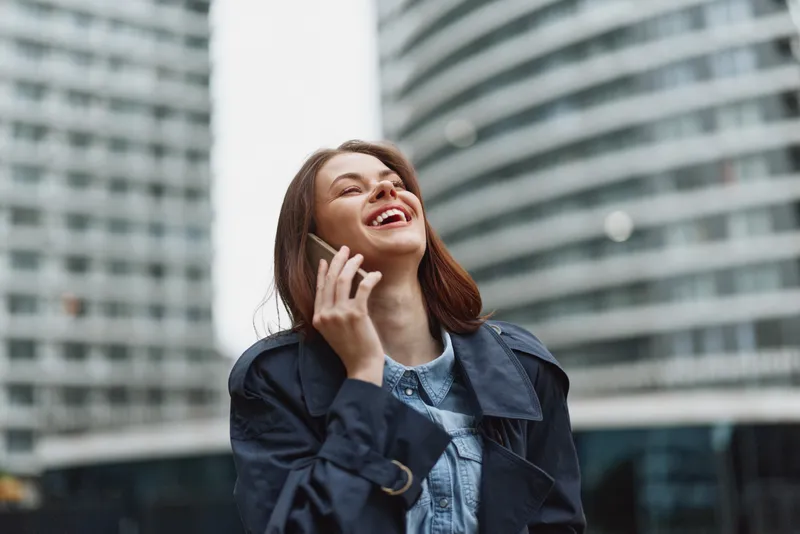 Urban professional on the phone, a brunette woman in a denim jacket stands on a busy city street backdrop, smiling confidently at the camera.