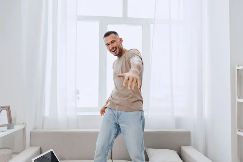 Young man joyfully expressing himself at home, surrounded by soft light and a relaxed atmosphere, highlighting themes of emotional minimalism and solo living.