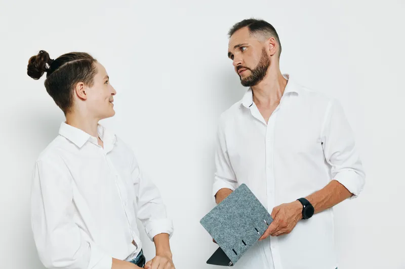 A professional male business figure stands with a colleague against an isolated white background, showing confident and thoughtful emotions during a calm, respectful discussion about strategy and