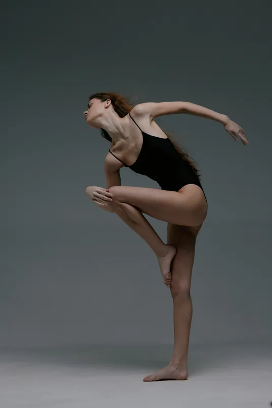 graceful woman dancer performing flexible pose in black leotard with neutral studio background