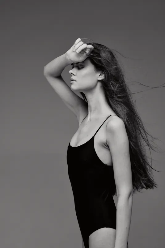 Black and white profile of a young woman with long hair in a black sleeveless outfit expressing calmness and elegance.