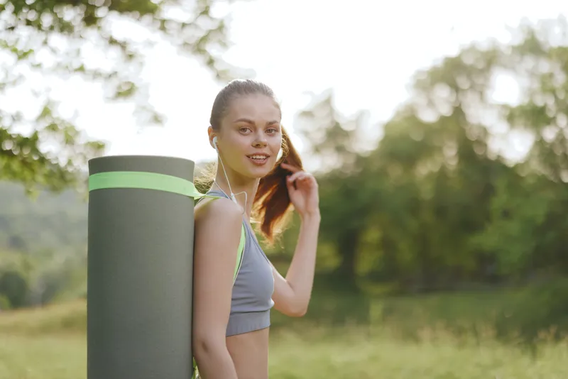 Young woman with yoga mat in a sunny outdoor setting, depicting health and wellness, confidence, and a connection to nature