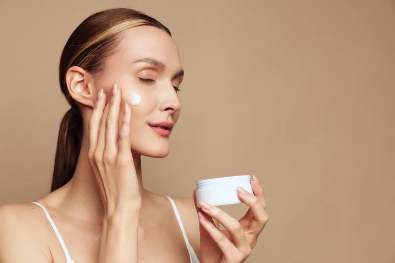Woman skincare, face cream and moisturizer, beauty spa care, holding cosmetic jar, young woman applies hydration on smooth skin, closeup on beige background