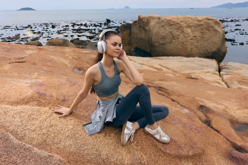Young woman enjoying music on rocky beach, wearing fitness attire, headphones, embodies relaxation and leisure, vibrant colors, ideal for wellness concepts