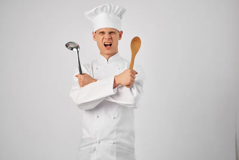 Мужчина в поварской форме с кухонной утварью профессионально готовит еду