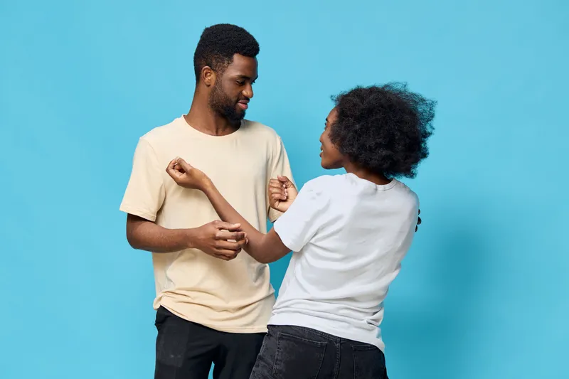 Joyful couple dancing together on a blue background, showcasing love and connection through movement and laughter, wearing casual clothes and expressing happiness
