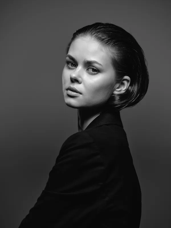 Black and white portrait of a serious woman with short hair in a dark outfit with dramatic lighting