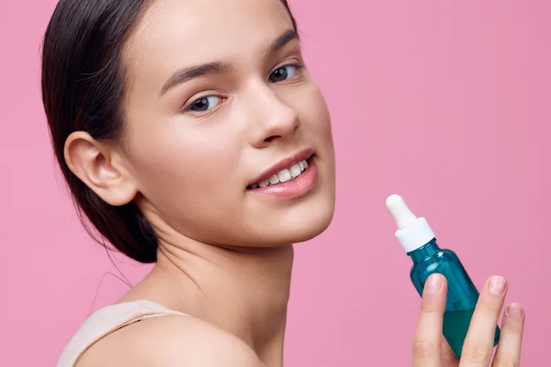 Beautiful young model applying skincare serum, smiling, with a pink background, emphasizing healthy skin and beauty KEY skincare, serum, beauty, model, healthy skin, smiling, pink background, cosme