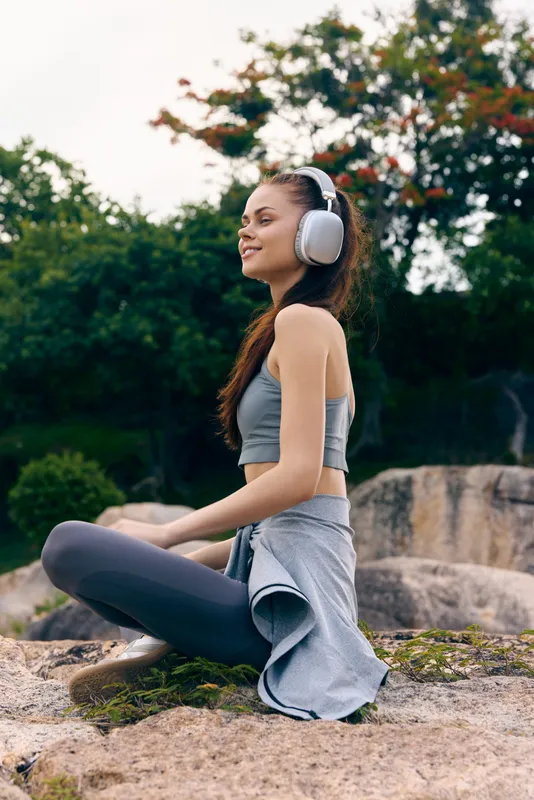 Young woman in active wear enjoying nature while listening to music with headphones outdoors, showcasing a relaxed and joyful attitude, ideal for wellness and fitness themes