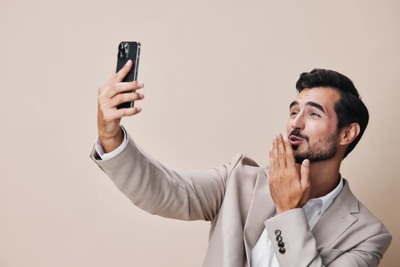 Улыбающийся мужчина в деловом костюме держит белый смартфон, делая селфи