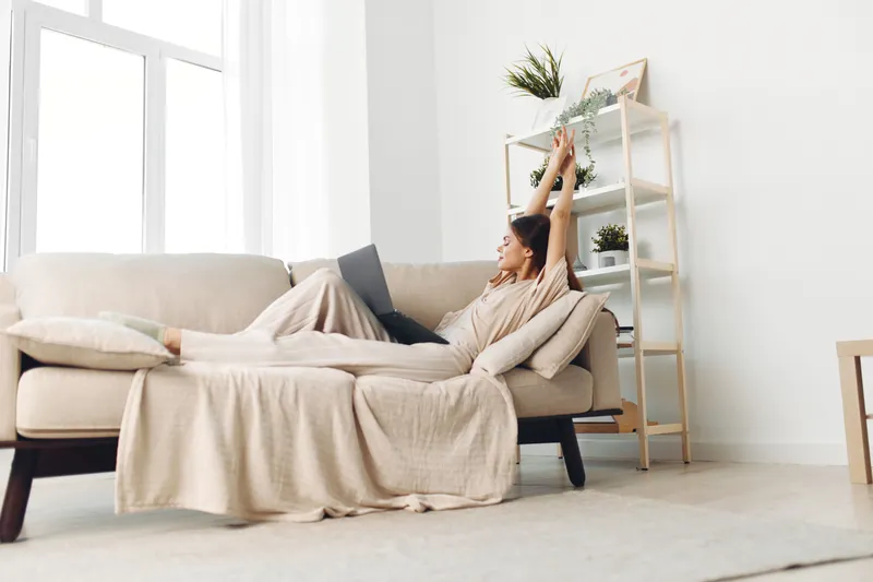 Улыбающаяся женщина печатает на ноутбуке в уютной гостиной, наслаждаясь фриланс-работой