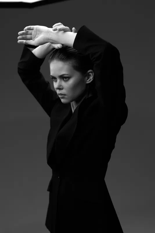 Black and white portrait of a serious woman posing with raised arms in stylish dark clothing