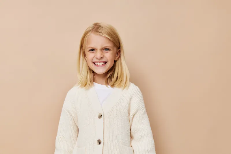 Эмоциональная девочка в модной детской одежде на бежевом фоне