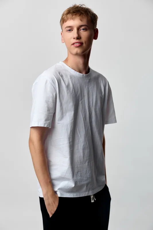 Male model in a white t shirt stands in a studio setting with a relaxed pose, clean background, simple fashion look, and casualwear vibe for lifestyle and apparel catalogs