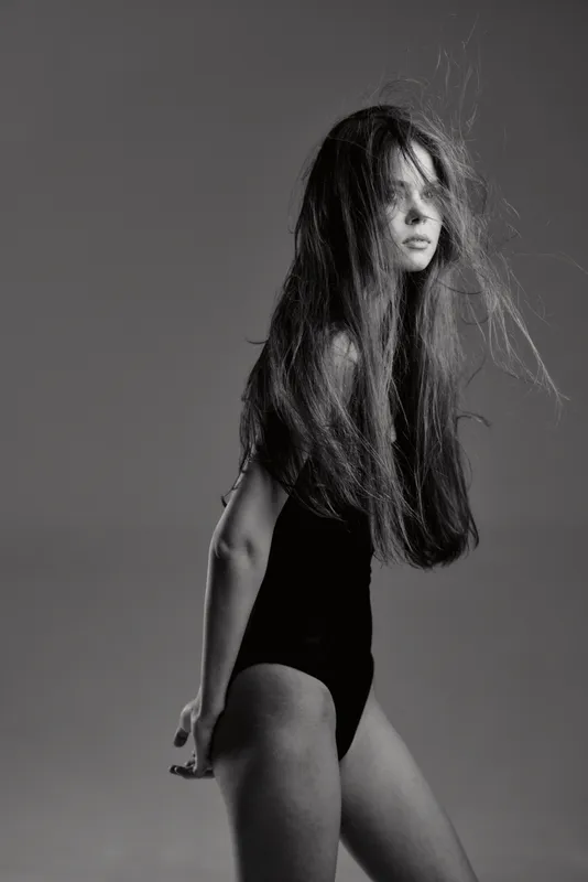Black and white portrait of a woman with long hair in a black bodysuit with flowing strands.