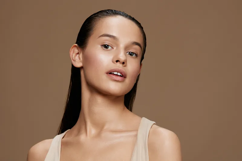 Young woman with smooth skin and natural makeup, showcasing confidence and beauty against a neutral brown background, perfect for beauty and skincare concepts