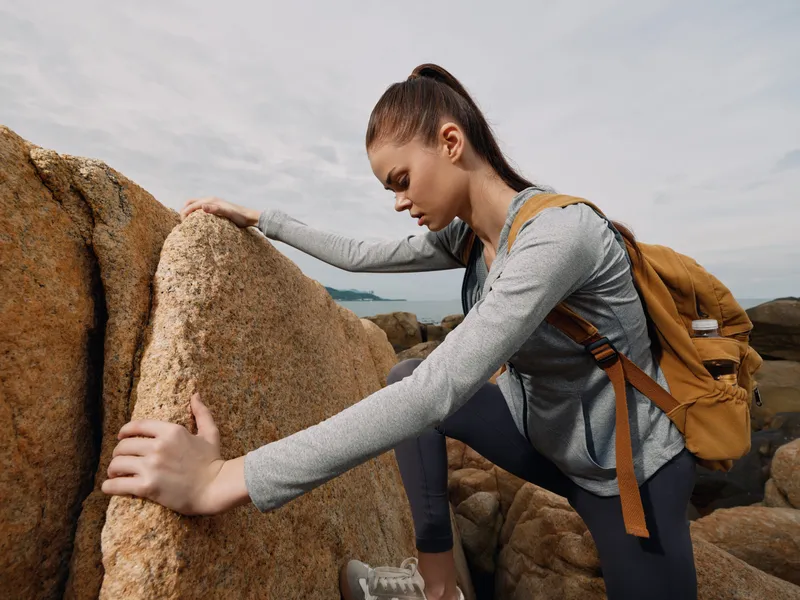 Young female hiker in activewear climbing rocky terrain, expressing determination and focus, with a natural background and earthy color palette