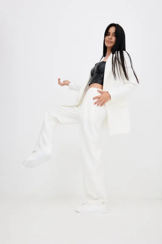 woman in white suit posing confidently with black top and sneakers in bright studio, showcasing modern fashion style with dynamic posture and casual elegance