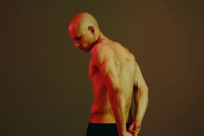 Muscular man posing back view in a dramatic light, showcasing strength and confidence. The ambiance creates a powerful atmosphere, emphasizing the human form beautifully.