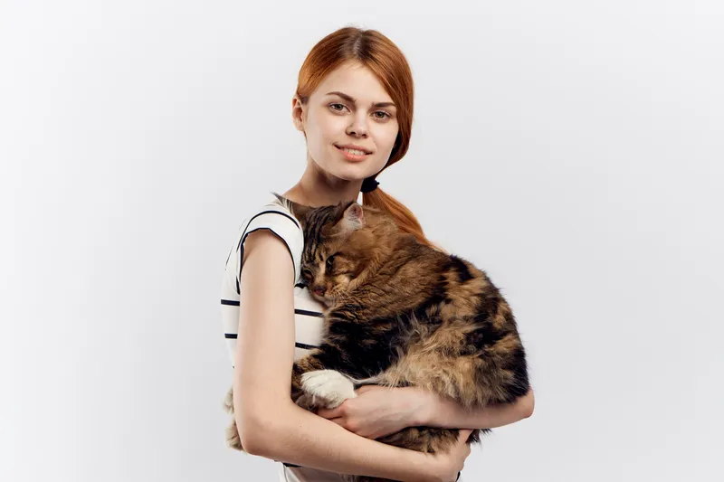 Рыжеволосая женщина держит в руке кота, полосатая футболка, светлый фон, дом, питомец