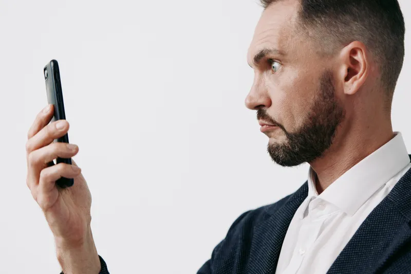 A professional business man stands in a focused pose, using a smartphone against a solid colored isolated background, conveying confidence, clarity, and readiness to communicate, lead projects, and